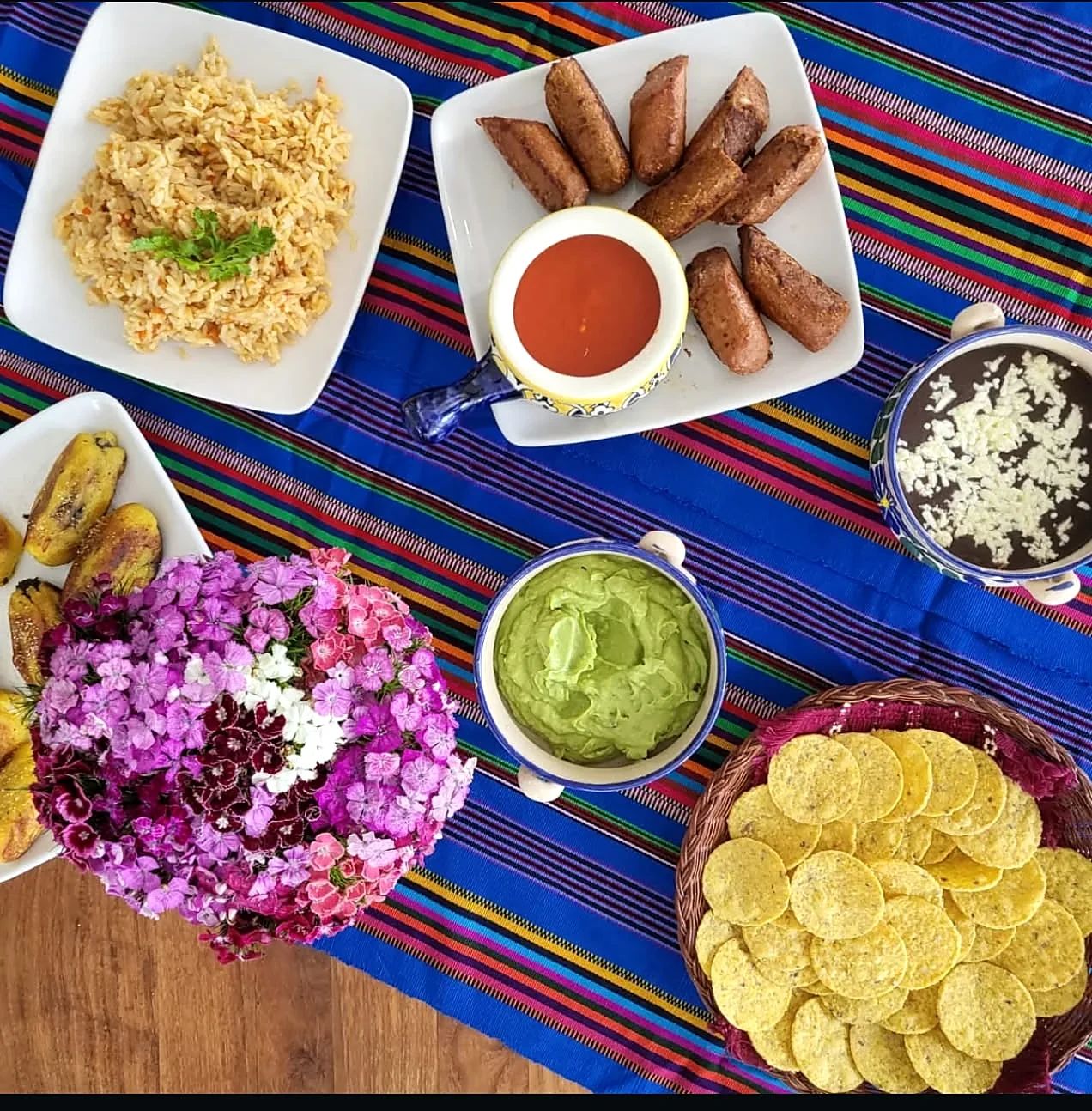 Mesa con arroz, plátanos fritos, frijoles, guacamole y totopos sobre un mantel típico de colores