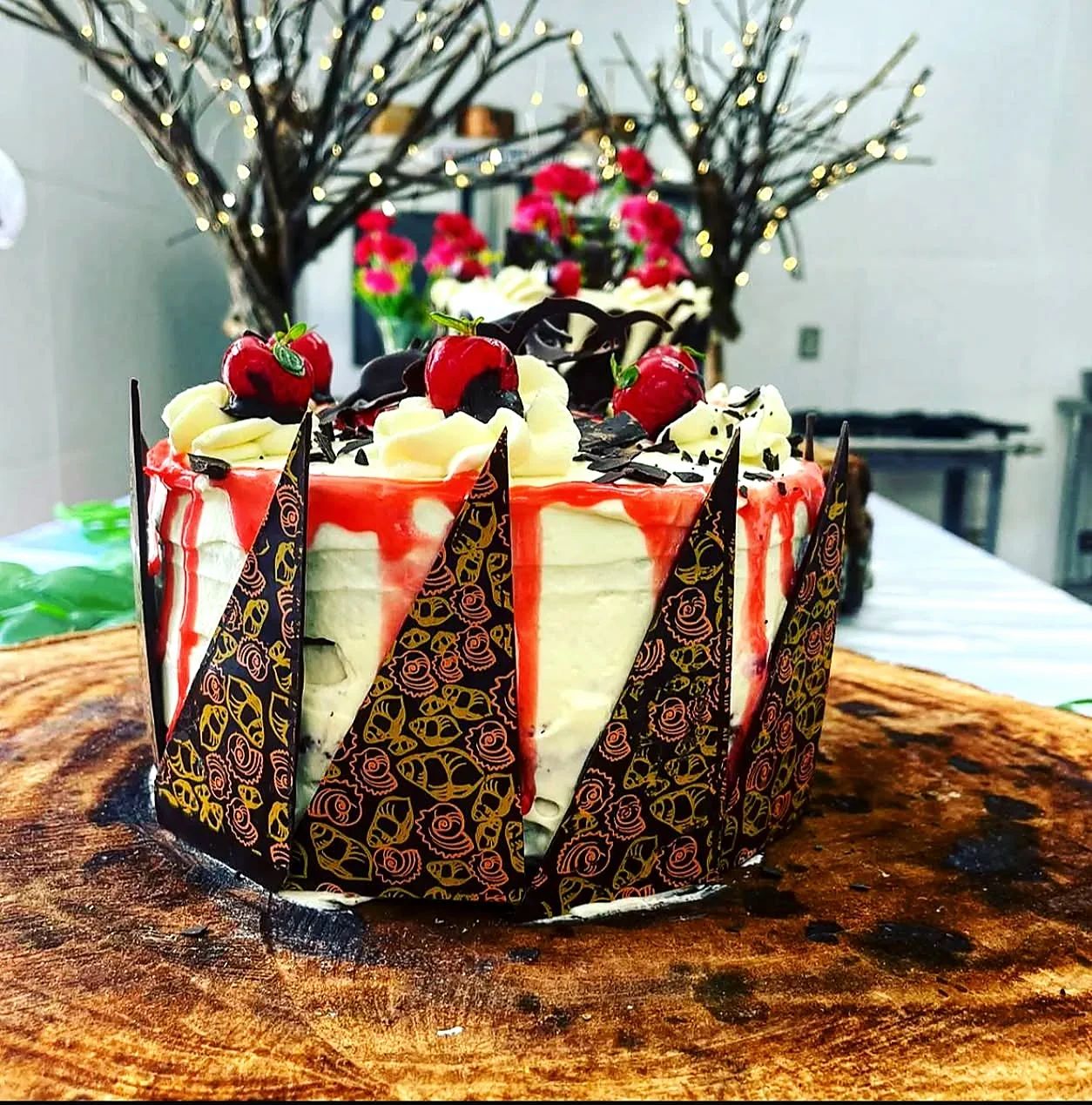 Pastel cremoso con cobertura roja, fresas y placas decorativas de chocolate