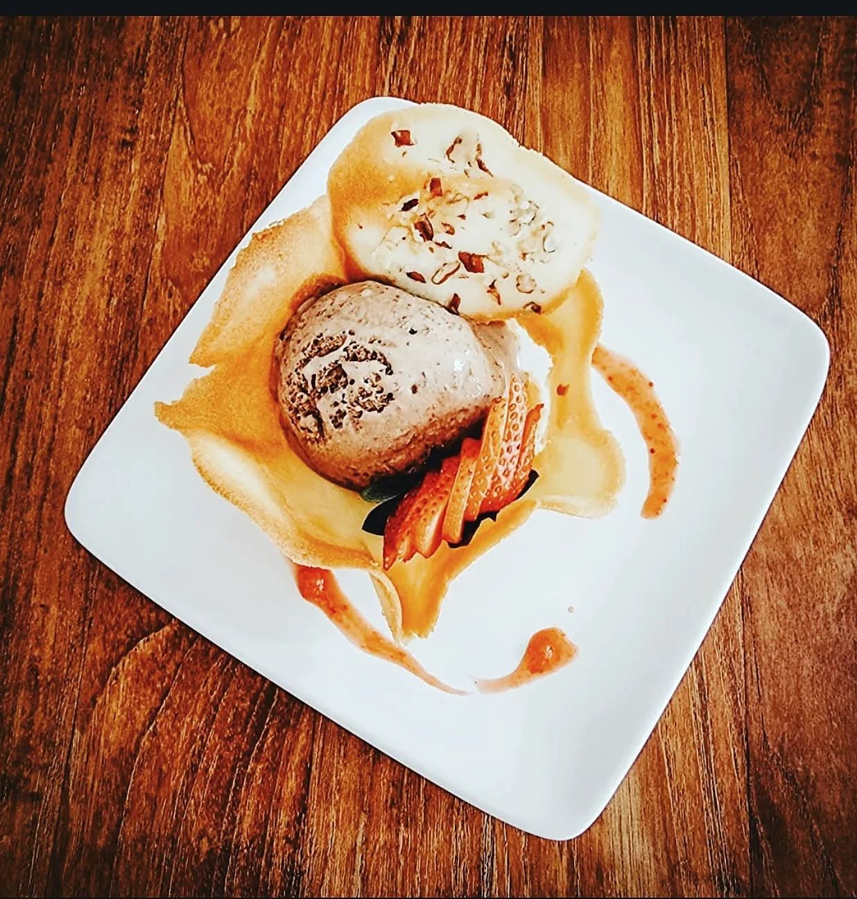 Bola de helado con fresas sobre una teja crujiente y salsa decorativa en plato blanco